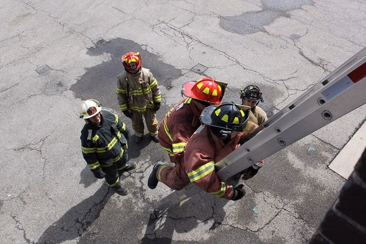 Why should a firefighter throw a ladder with a shallow angle?